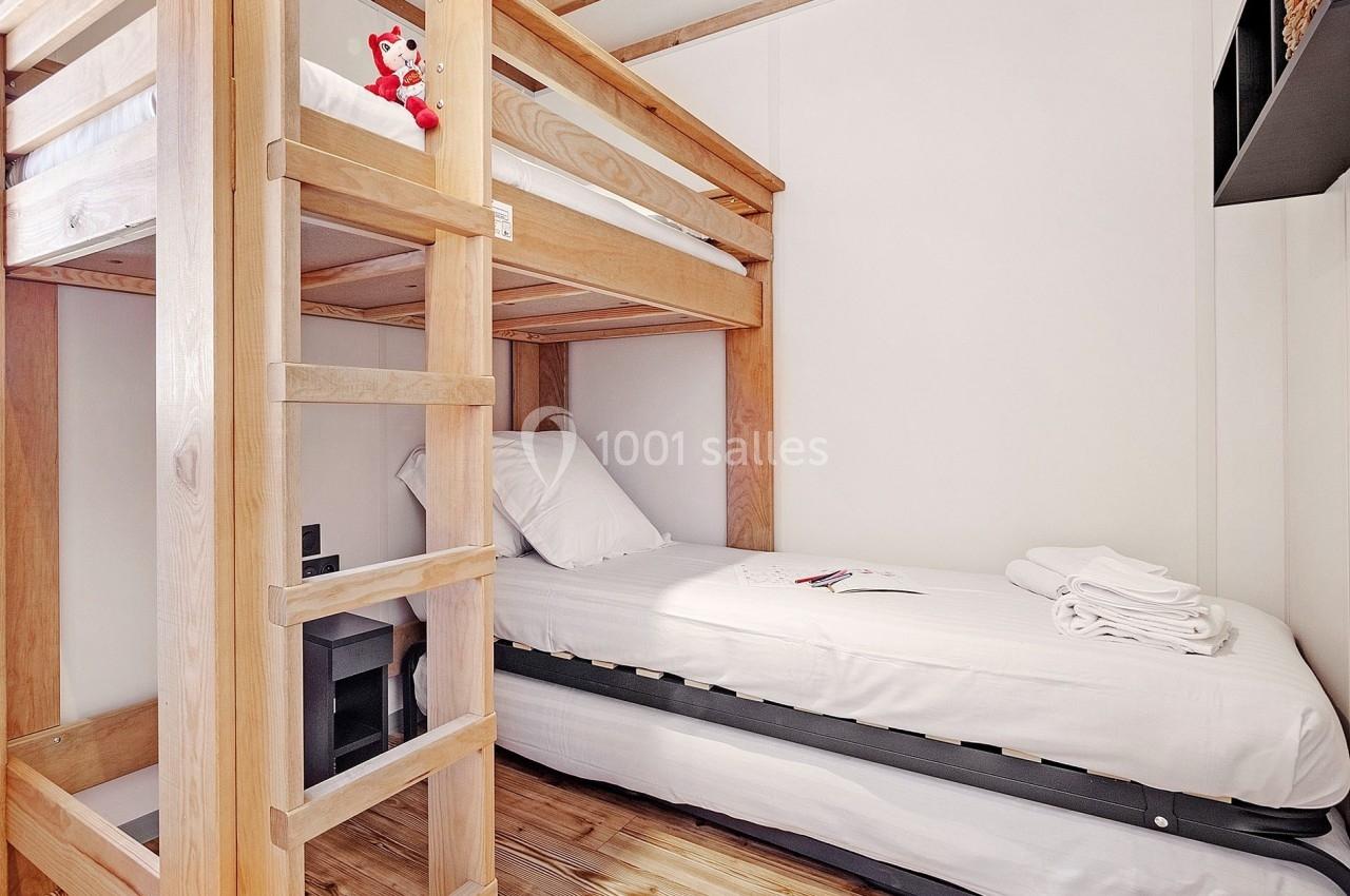 Lit superposé en bois clair avec un lit simple en dessous, dans une chambre lumineuse au sol en parquet.