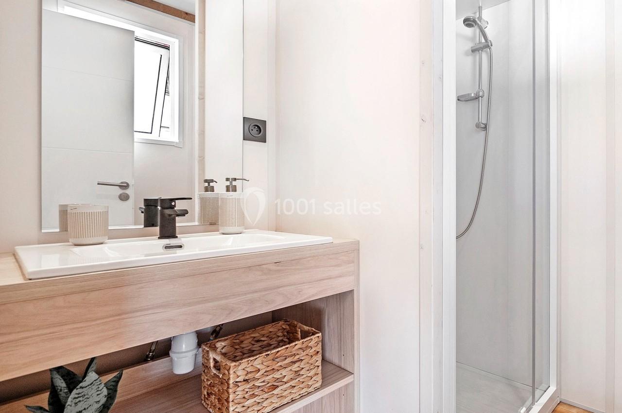 Salle de bain lumineuse avec un meuble en bois, un lavabo moderne, un panier en osier et une cabine de douche vitrée.