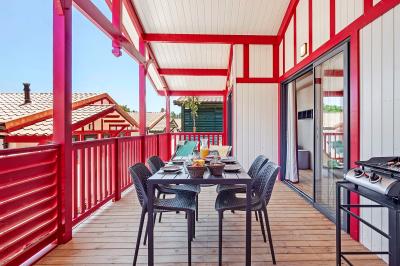 Terrasse en bois avec table dressée, chaises noires, barbecue et vue sur des maisons à colombages rouges et blanches.