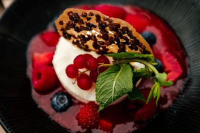Terrasse en bois avec table dressée, chaises noires, barbecue et vue sur des maisons à colombages rouges et blanches.