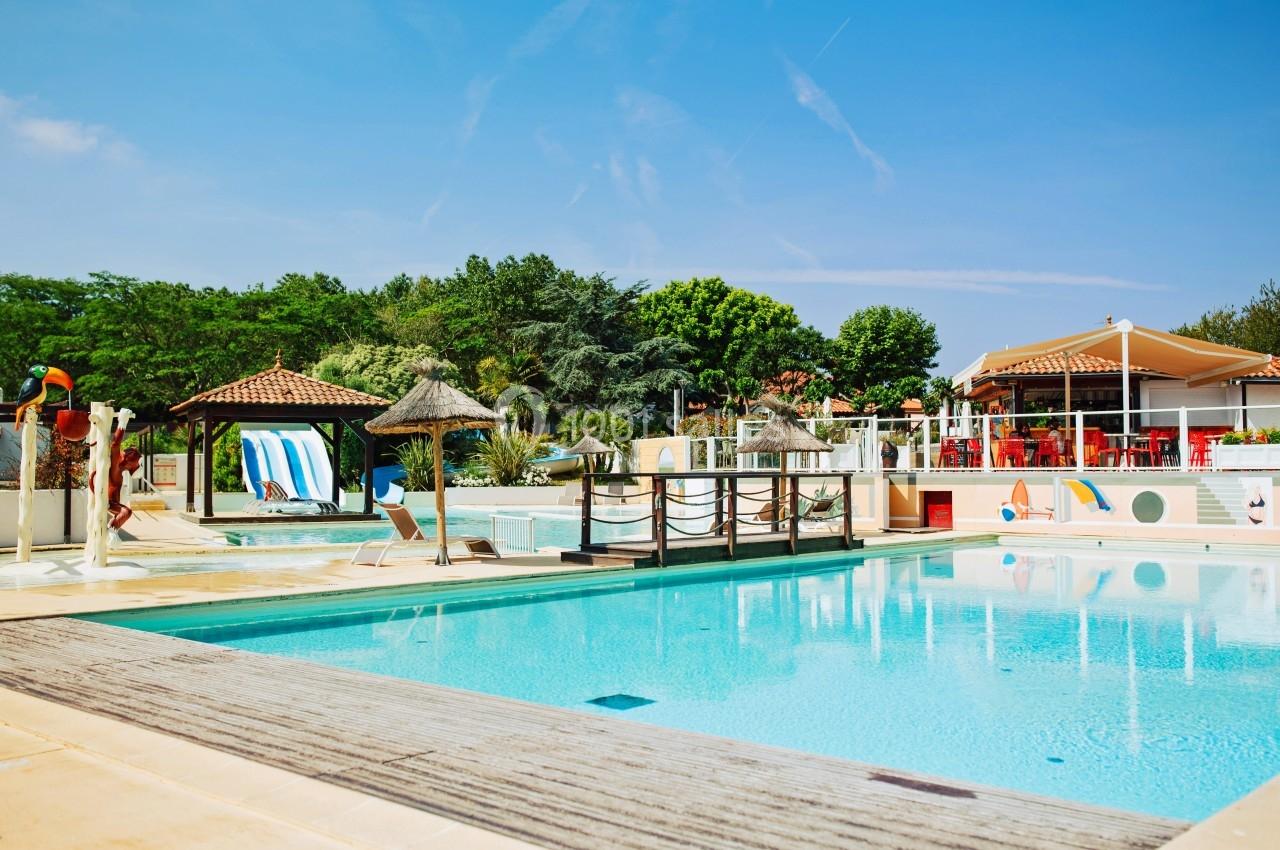 Piscine extérieure avec parasols en chaume, toboggans et terrasse de restaurant sous un ciel dégagé.
