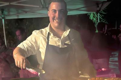 Terrasse en bois avec table dressée, chaises noires, barbecue et vue sur des maisons à colombages rouges et blanches.