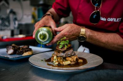 Terrasse en bois avec table dressée, chaises noires, barbecue et vue sur des maisons à colombages rouges et blanches.