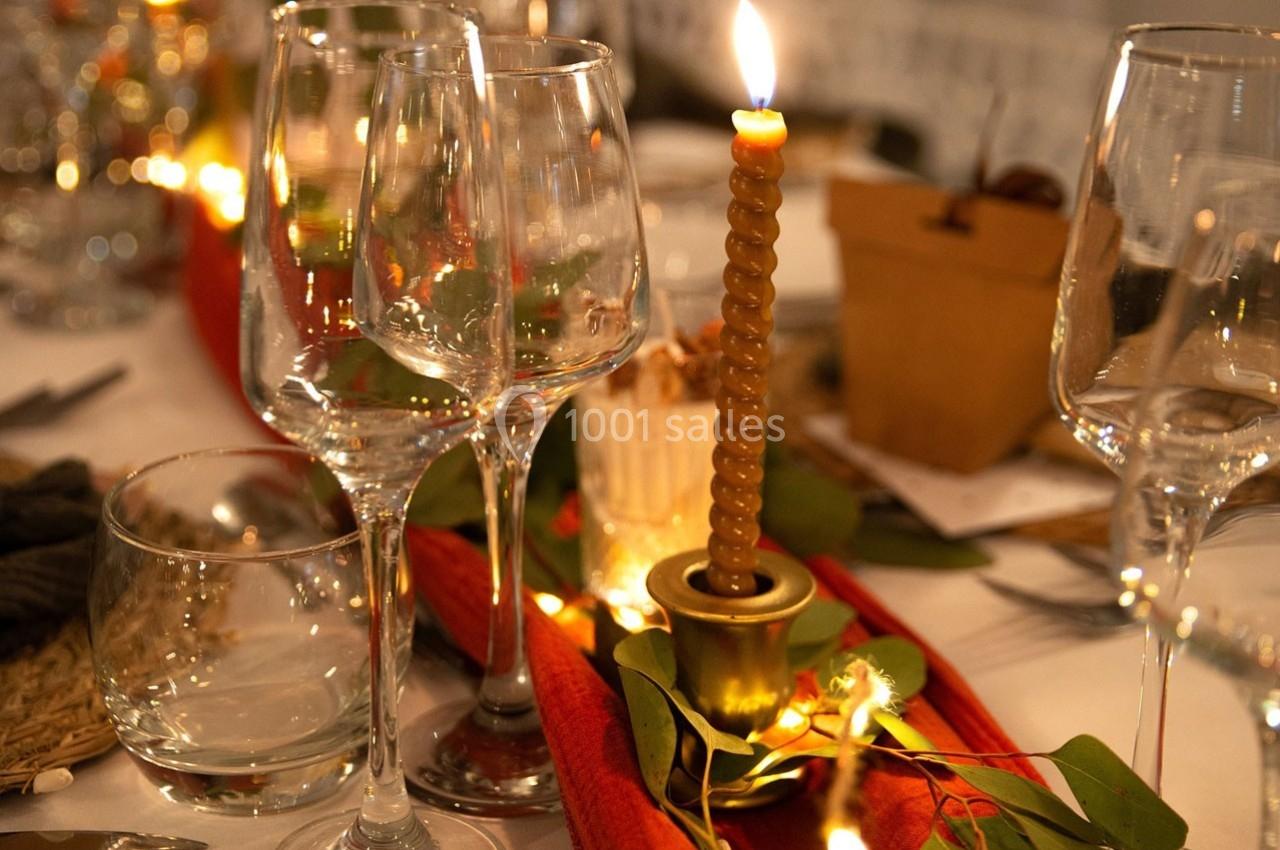 Bougie allumée au centre d'une table décorée avec des verres, feuillage et guirlandes lumineuses.