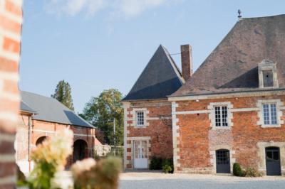 Cour pavée avec un bâtiment en briques rouges et toit en ardoise, entouré de végétation sous un ciel bleu.
