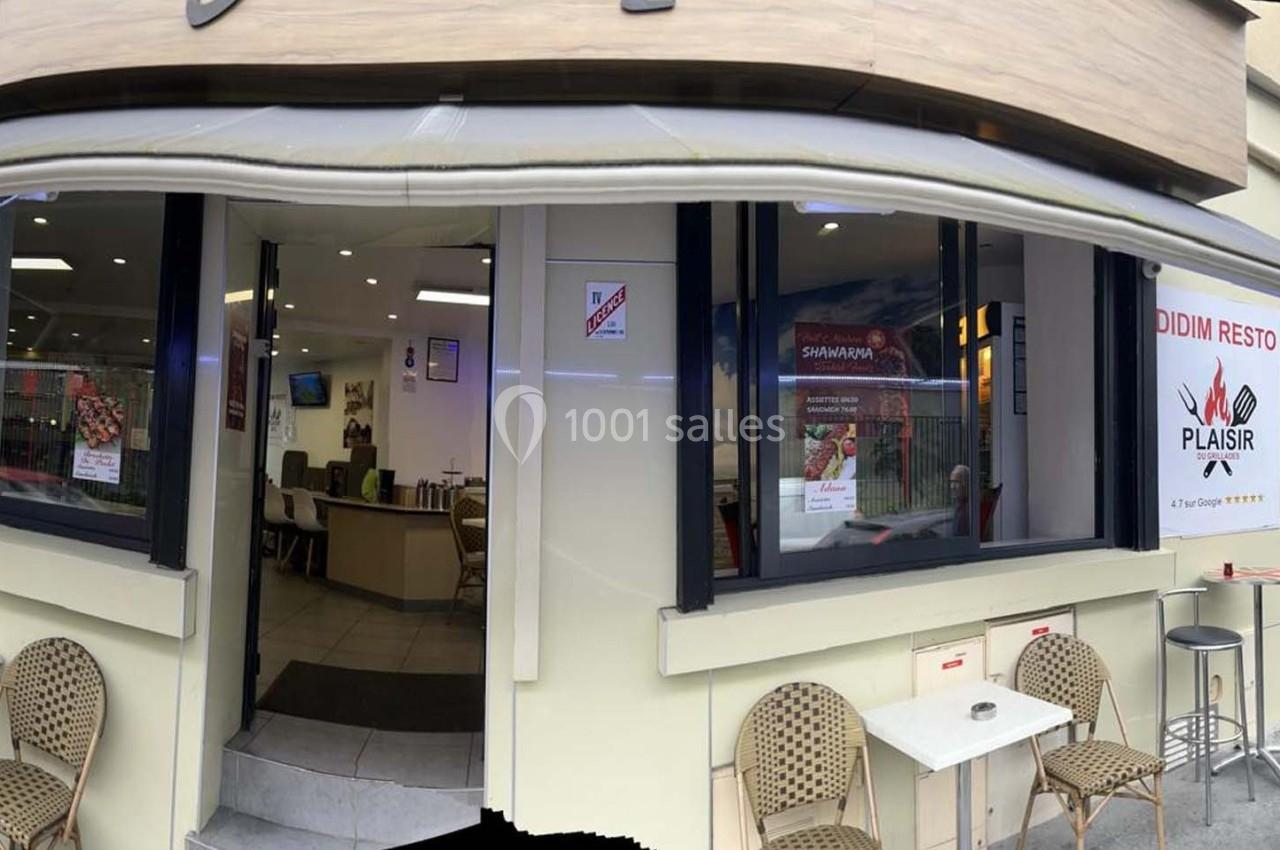 Façade d'un restaurant avec terrasse équipée de chaises en rotin, entrée vitrée et enseignes visibles.