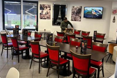 Salle de restaurant lumineuse avec tables et chaises rouges, un client assis et un employé au comptoir.