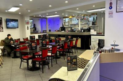 Salle de restaurant lumineuse avec tables et chaises rouges, un client assis et un employé au comptoir.