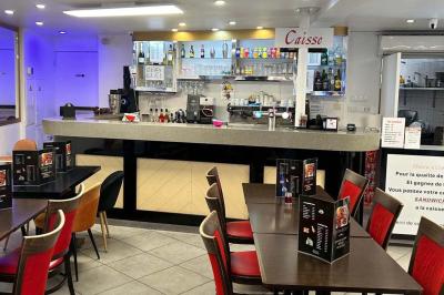 Salle de restaurant lumineuse avec tables et chaises rouges, un client assis et un employé au comptoir.