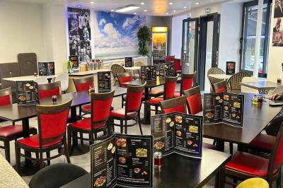 Salle de restaurant lumineuse avec tables et chaises rouges, un client assis et un employé au comptoir.