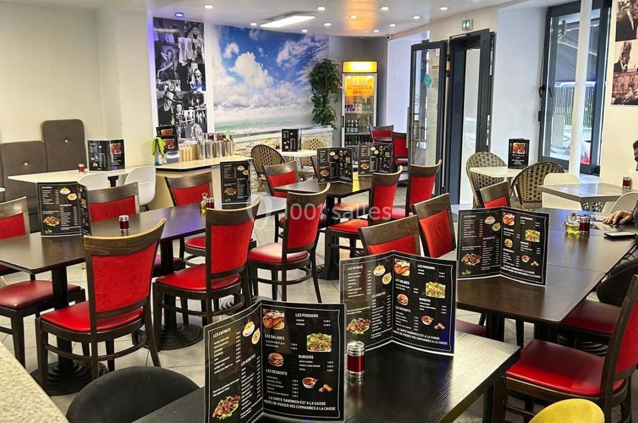 Salle de restaurant lumineuse avec des tables dressées, des chaises rouges et un décor mural représentant une plage.