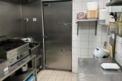 Salle de restaurant lumineuse avec tables et chaises rouges, un client assis et un employé au comptoir.