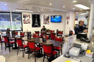Salle de restaurant lumineuse avec tables et chaises rouges, un client assis et un employé au comptoir.