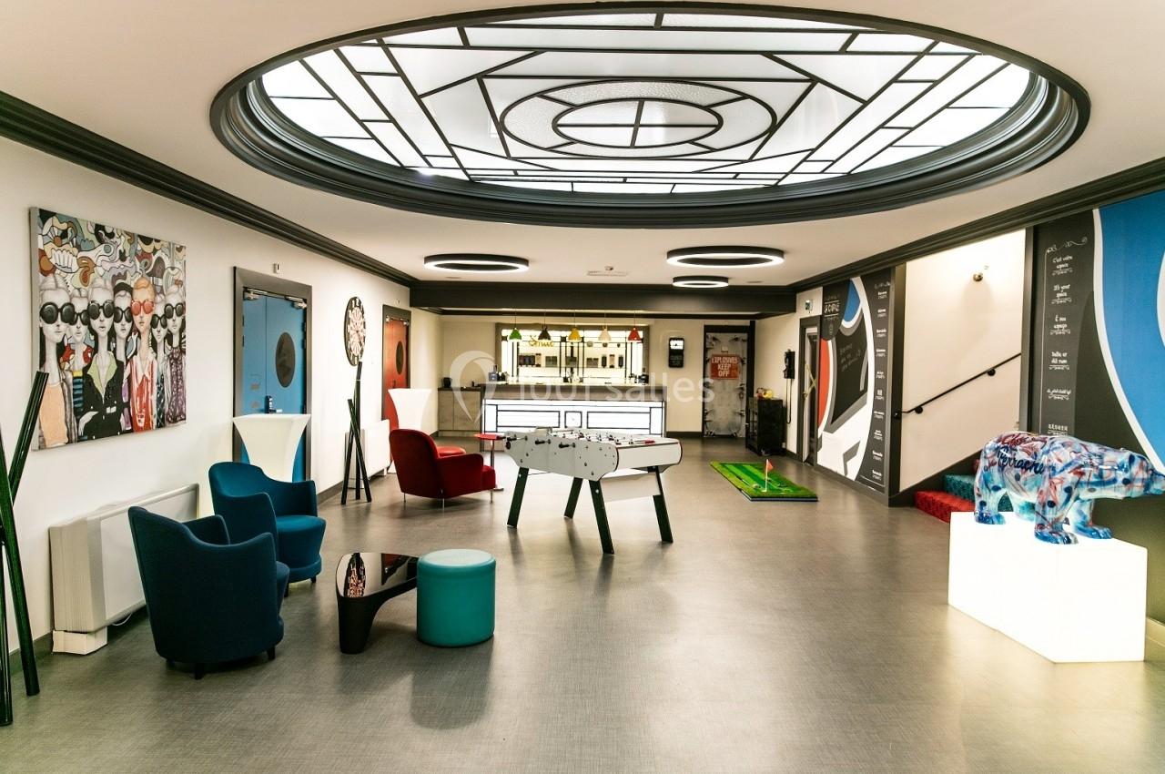 Espace intérieur moderne avec baby-foot, fauteuils colorés, œuvres d'art et comptoir de bar en arrière-plan.
