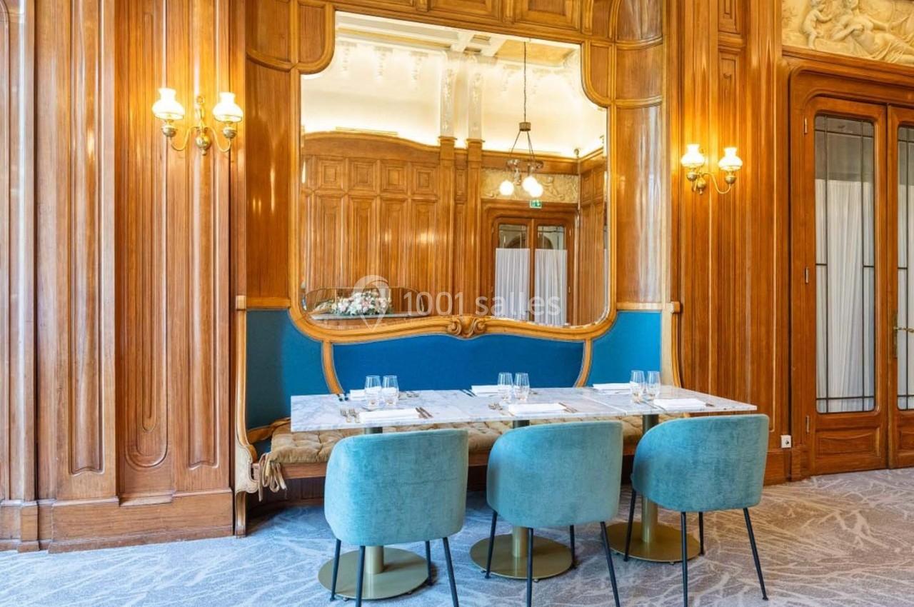 Salle à manger élégante avec table dressée, chaises en velours bleu et boiseries murales ornées d'un grand miroir.