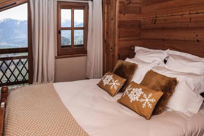 Chambre en bois avec lit double, coussins décoratifs et vue sur les montagnes enneigées par une fenêtre et un balcon.
