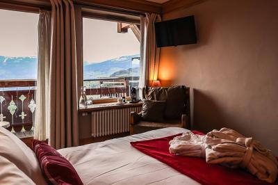 Chambre en bois avec lit double, coussins décoratifs et vue sur les montagnes enneigées par une fenêtre et un balcon.