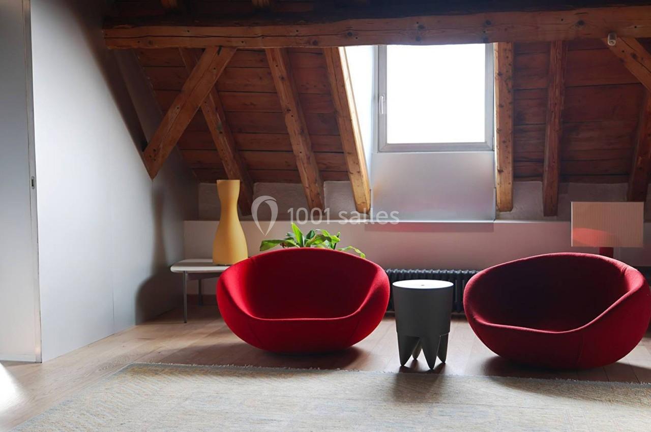 Deux fauteuils rouges arrondis placés sous un toit en bois avec une fenêtre, entourés de décorations minimalistes.