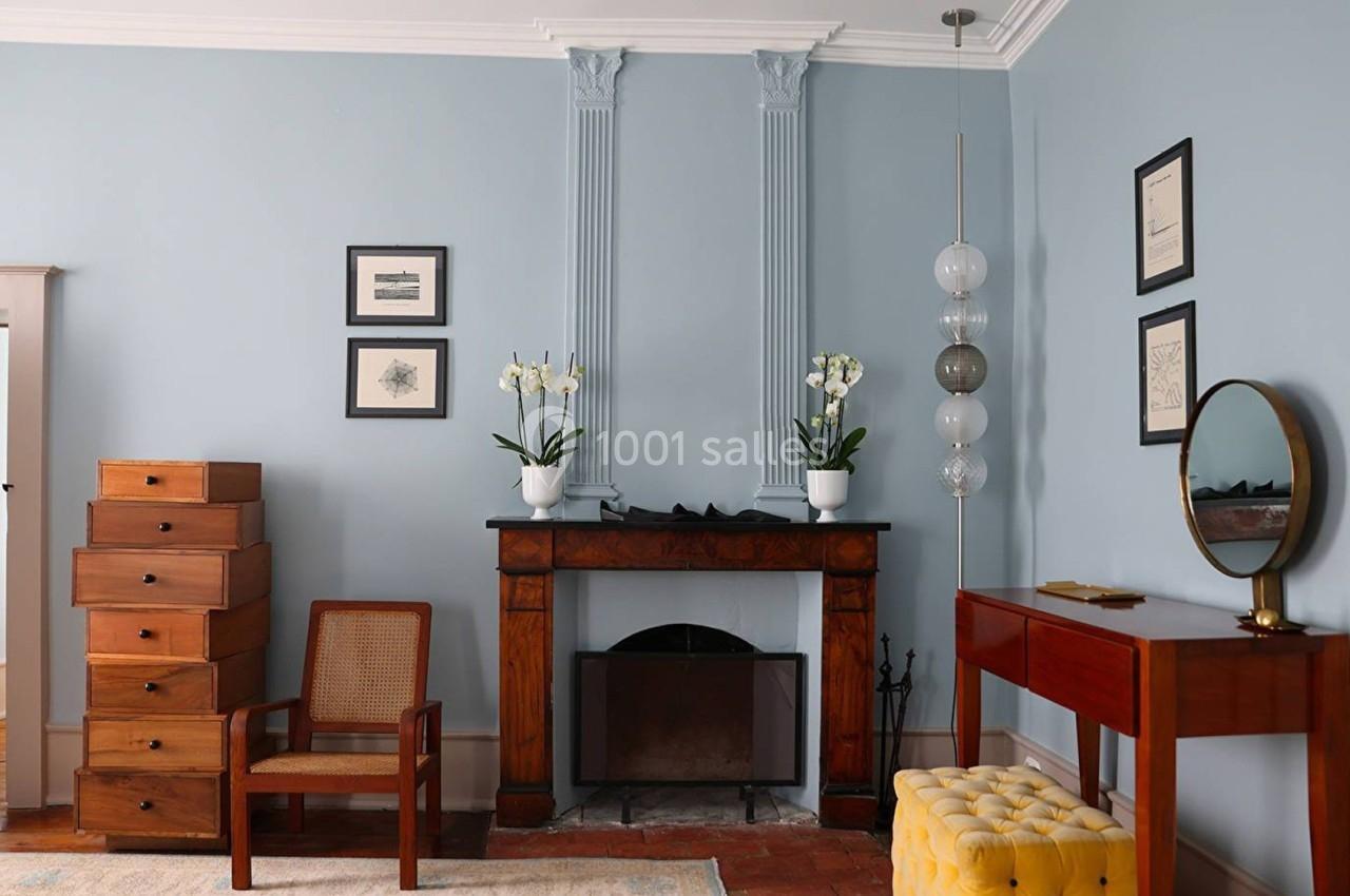 Salon avec murs bleus, cheminée en bois, meubles vintage, orchidées blanches et décoration murale encadrée.