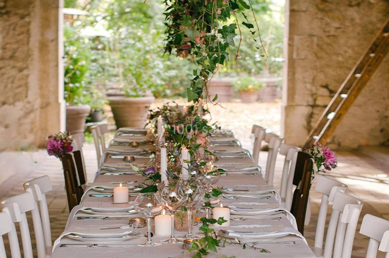 Table décorée avec des bougies, fleurs et feuillage, installée dans un espace rustique avec murs en pierre et lumière…