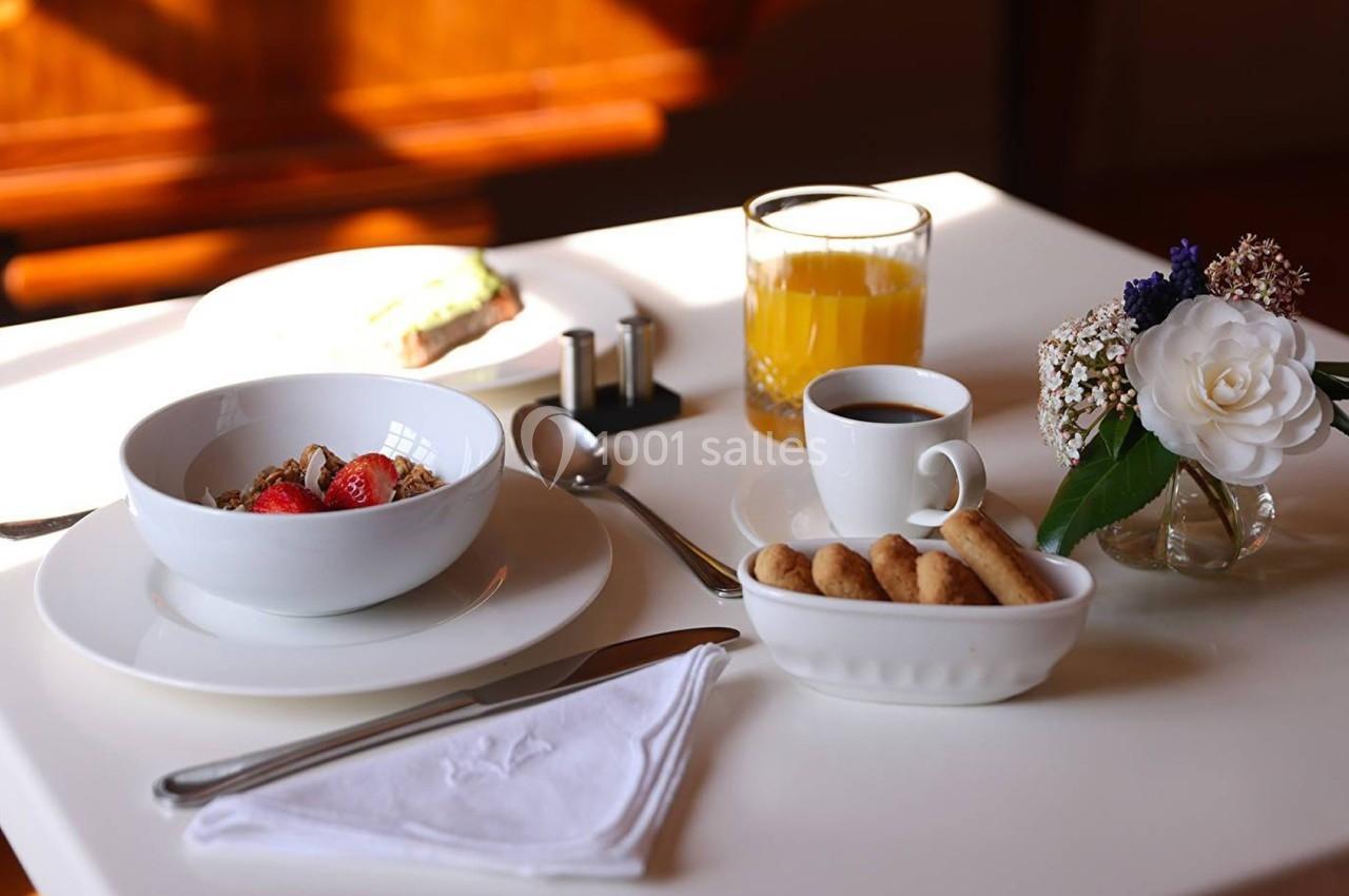 Petit-déjeuner servi sur une table avec bol de céréales, café, jus d'orange, biscuits et petite composition florale.
