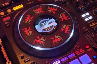 Table de mixage DJ avec platines, boutons lumineux, écran tactile et microphone sur une scène éclairée.