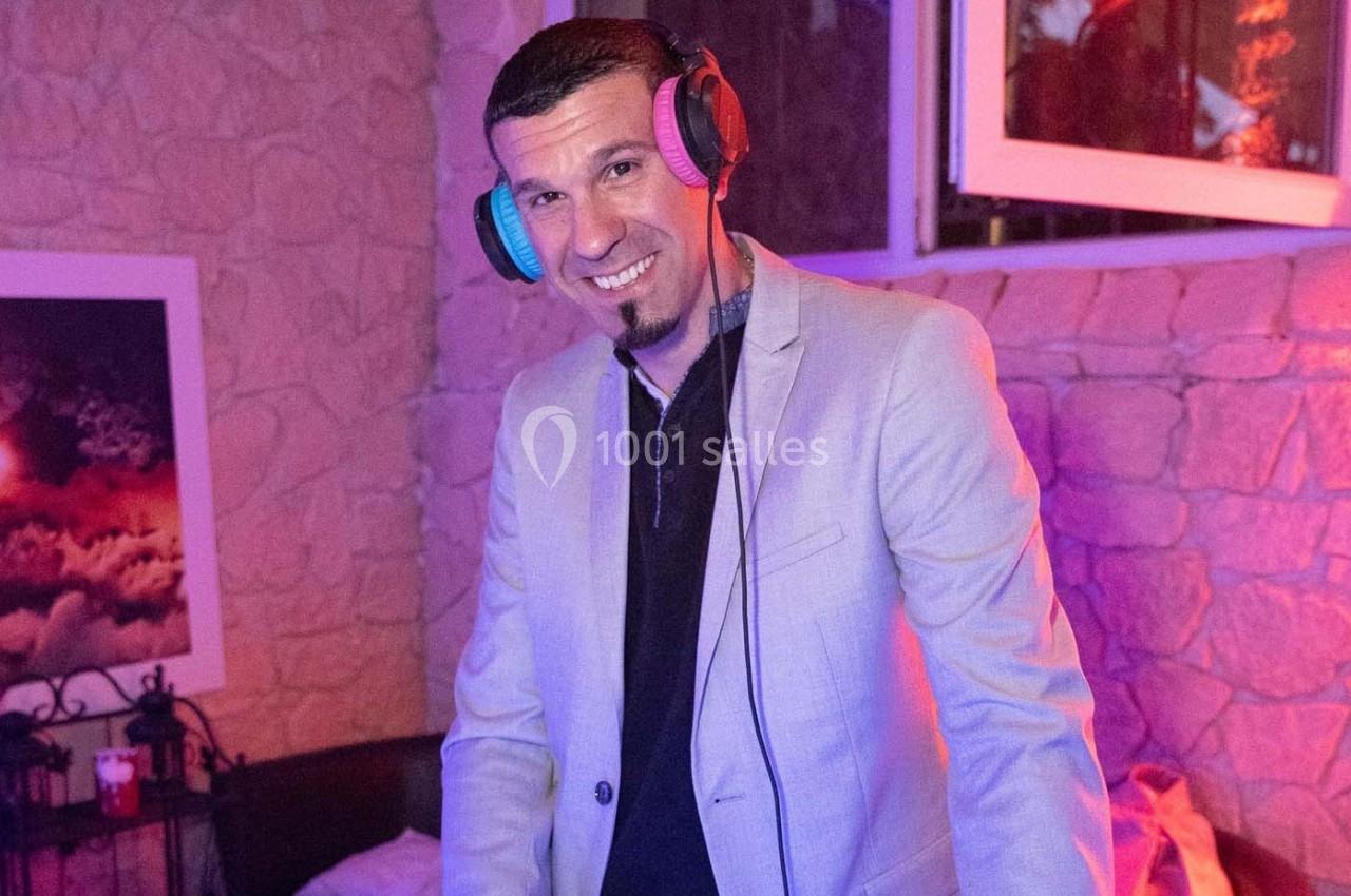 Homme souriant portant un casque audio, vêtu d'une veste claire, dans un intérieur à éclairage coloré.