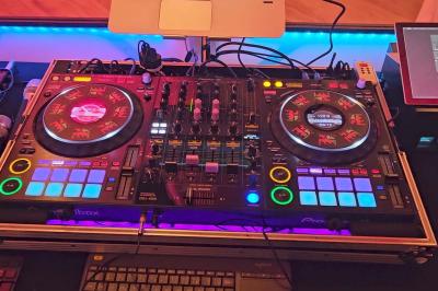 Table de mixage DJ avec platines, boutons lumineux, écran tactile et microphone sur une scène éclairée.