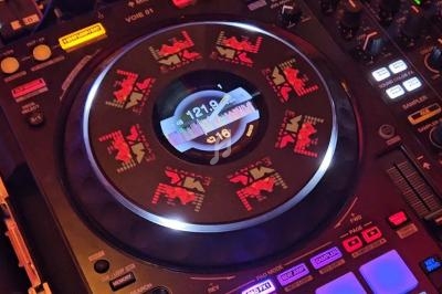 Platine DJ avec écran central affichant des informations de lecture et des motifs lumineux rouges et noirs.