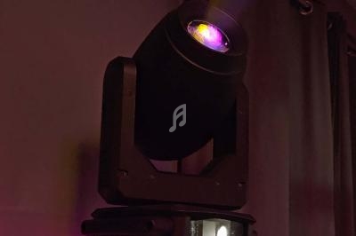 Projecteur LED orientable émettant une lumière violette dans une pièce sombre avec des rideaux en arrière-plan.