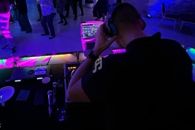 Un DJ de dos mixe de la musique sur une table de mixage éclairée, avec des personnes dansant en arrière-plan.
