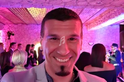 Homme souriant prenant un selfie dans une salle éclairée de lumières colorées, avec des personnes en arrière-plan.