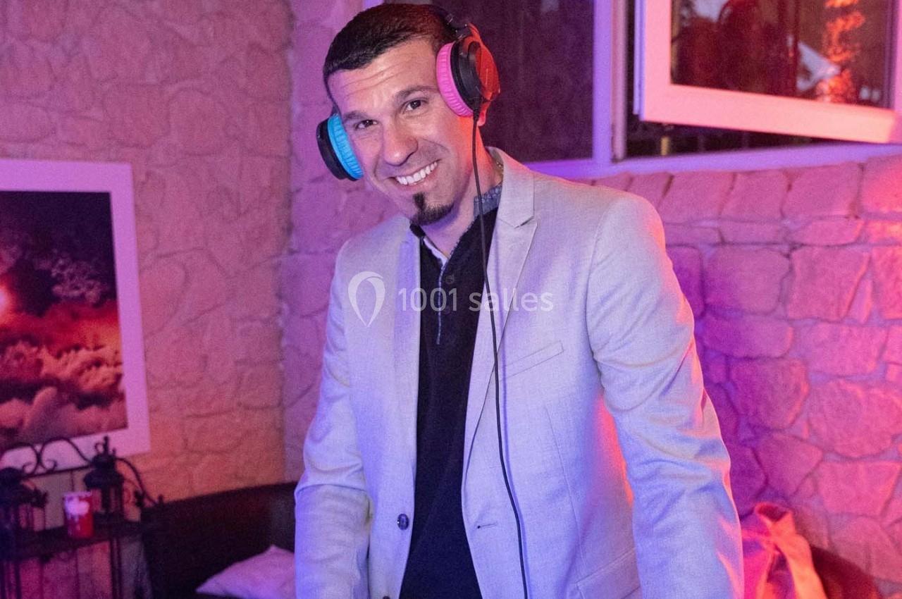 Homme souriant portant un casque audio, debout dans une pièce éclairée par des lumières colorées.