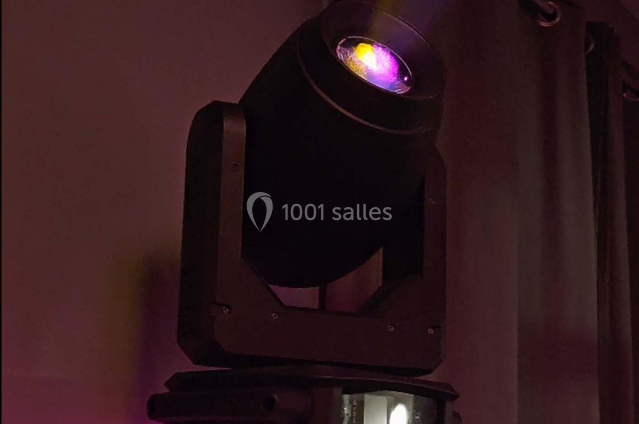 Projecteur lumineux noir émettant une lumière violette dans un environnement sombre avec des rideaux en arrière-plan.