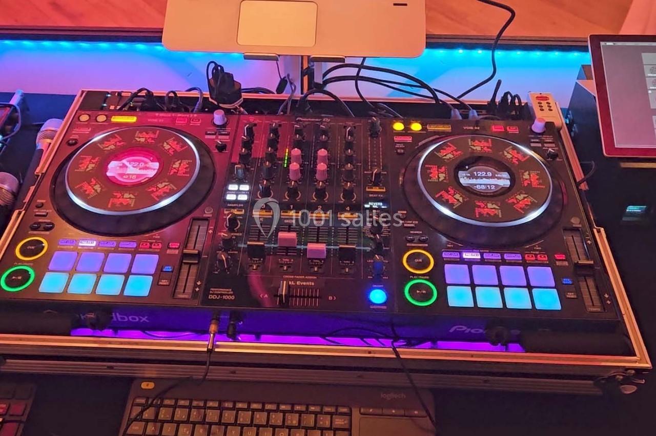Table de mixage DJ avec platines, boutons lumineux, écran tactile et microphone sur une scène éclairée.