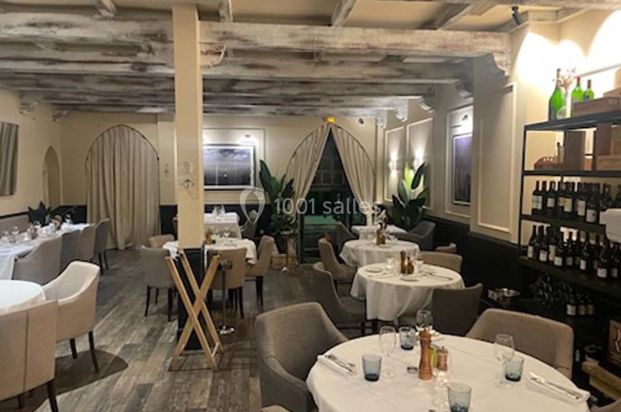 Salle de restaurant élégante avec tables dressées, chaises confortables, étagères à vin et éclairage chaleureux.