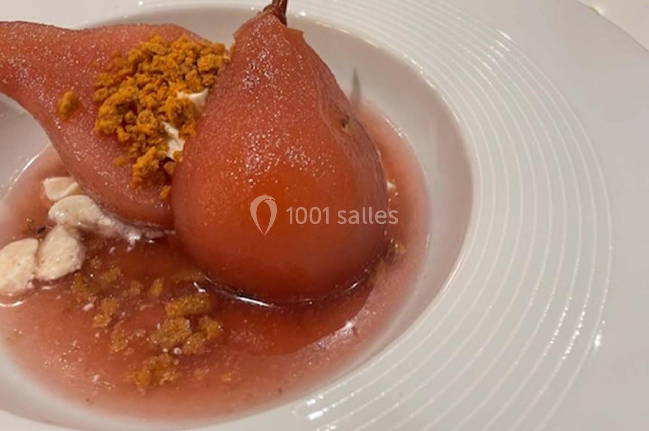 Poires pochées au sirop rouge servies avec des éclats croustillants et une garniture crémeuse dans une assiette blanche.