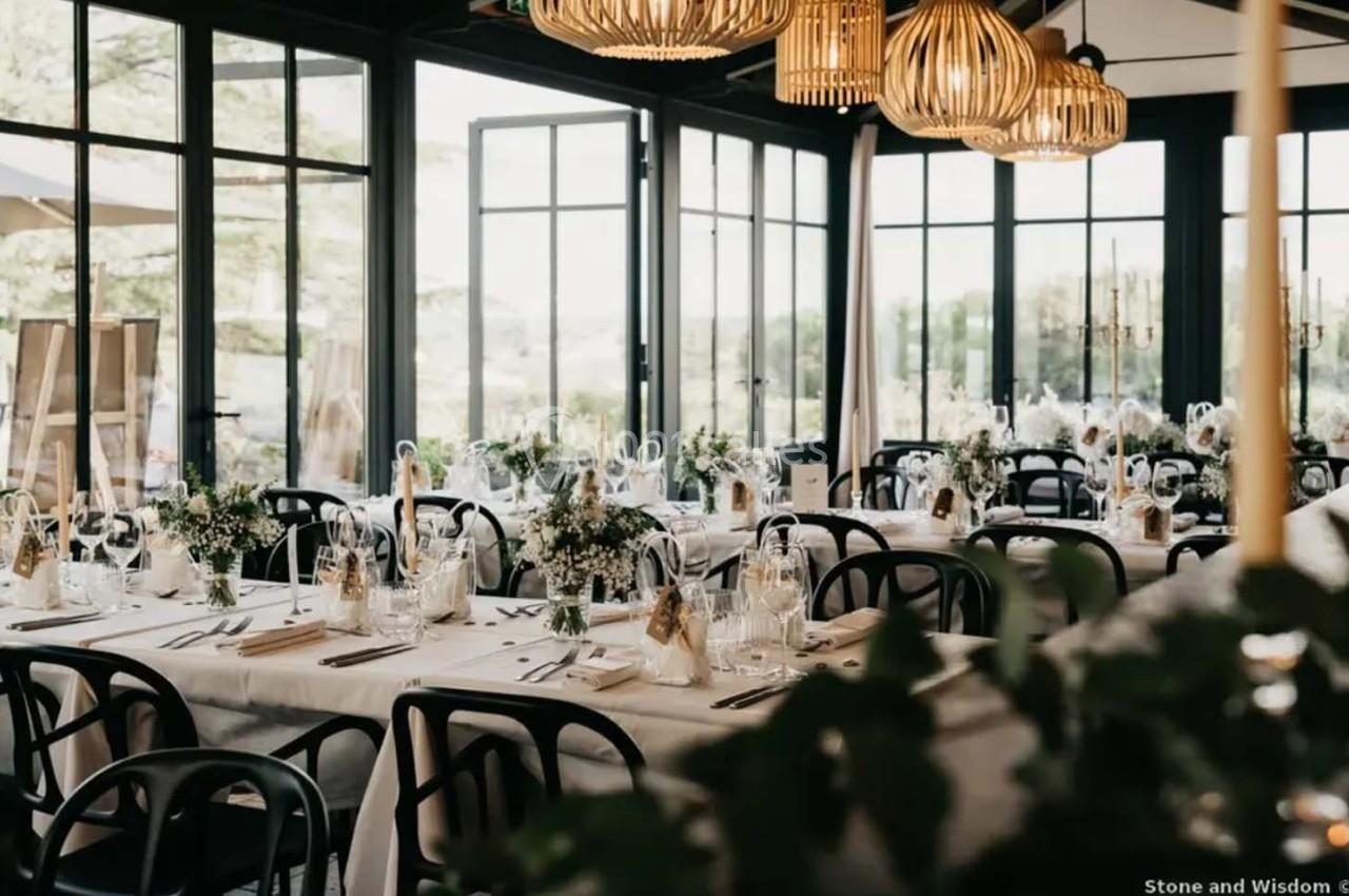 Salle de réception lumineuse avec tables dressées, décorations florales et suspensions en osier.