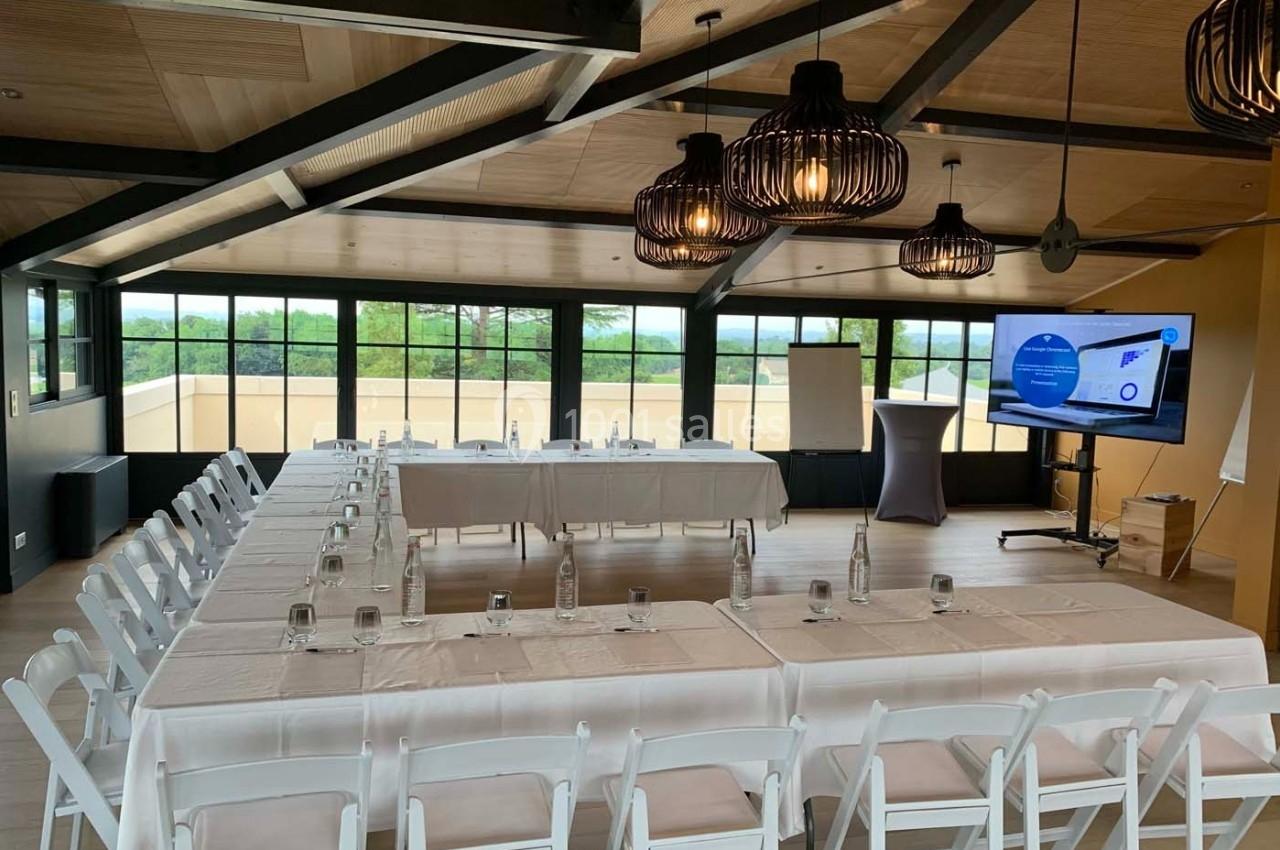 Salle de réunion lumineuse avec tables en U, chaises blanches, écran de présentation et vue sur l'extérieur.