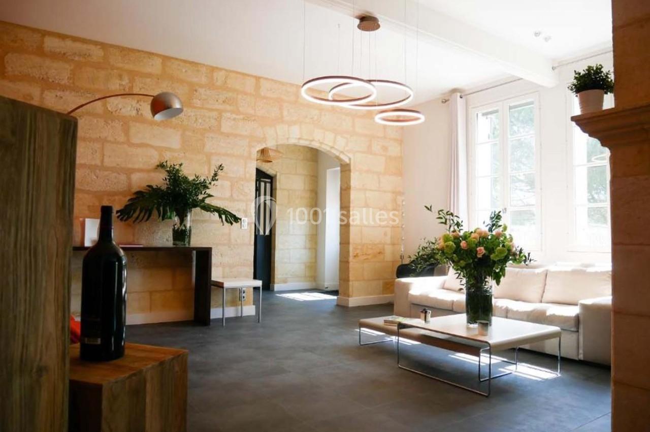 Salon lumineux avec murs en pierre, canapé blanc, table basse, plantes et suspensions modernes.