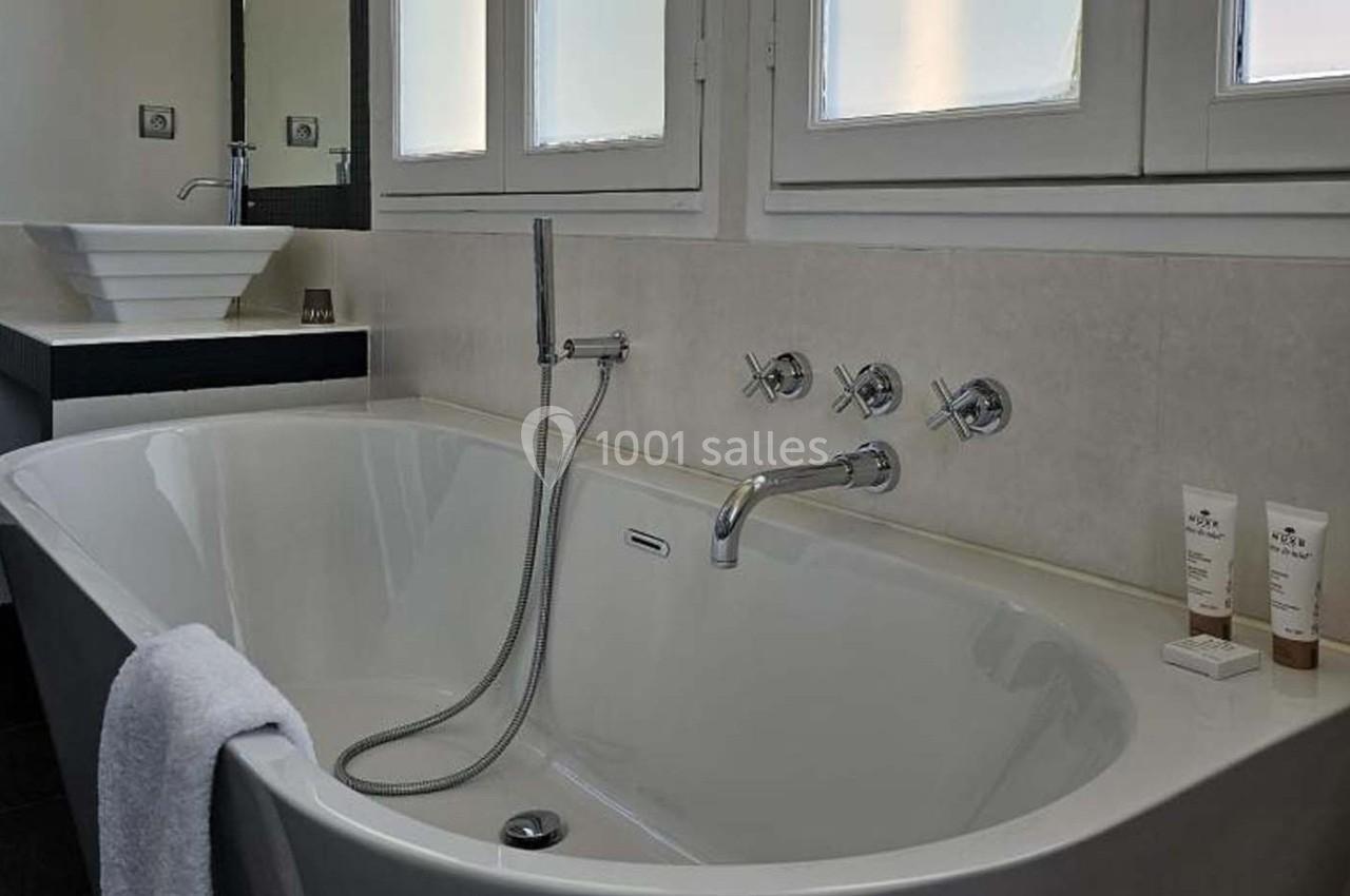 Baignoire blanche avec robinetterie moderne, serviette accrochée et produits de soin posés sur le rebord.