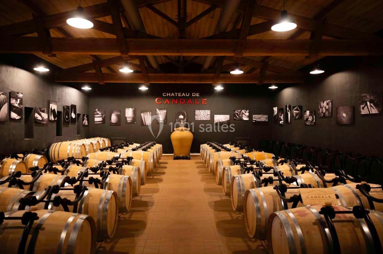 Salle de vieillissement avec des rangées de barriques en bois alignées sous un plafond en poutres apparentes.