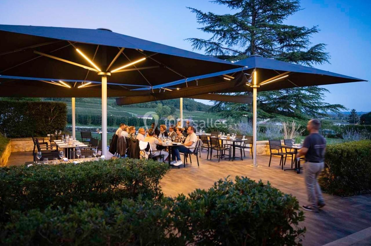 Terrasse extérieure d'un restaurant au crépuscule, avec des convives attablés sous de grands parasols éclairés.