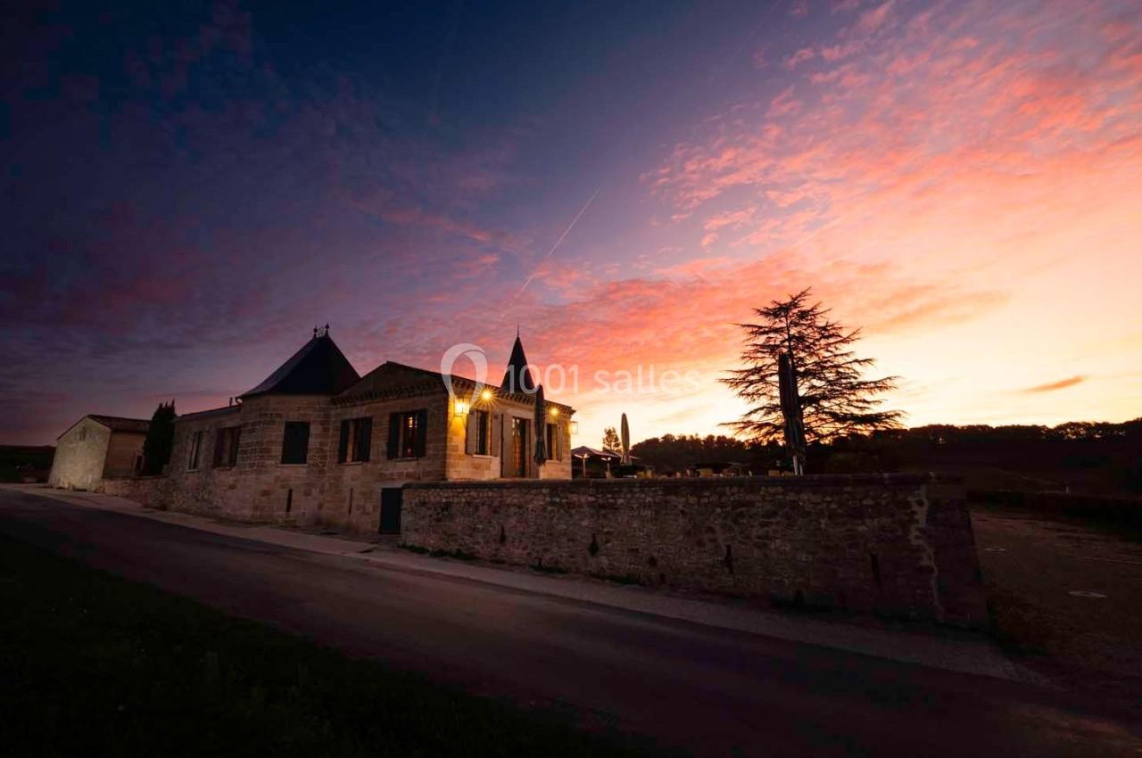 Bâtiment en pierre avec une tour, éclairé au crépuscule, sous un ciel coloré de nuances roses et violettes.