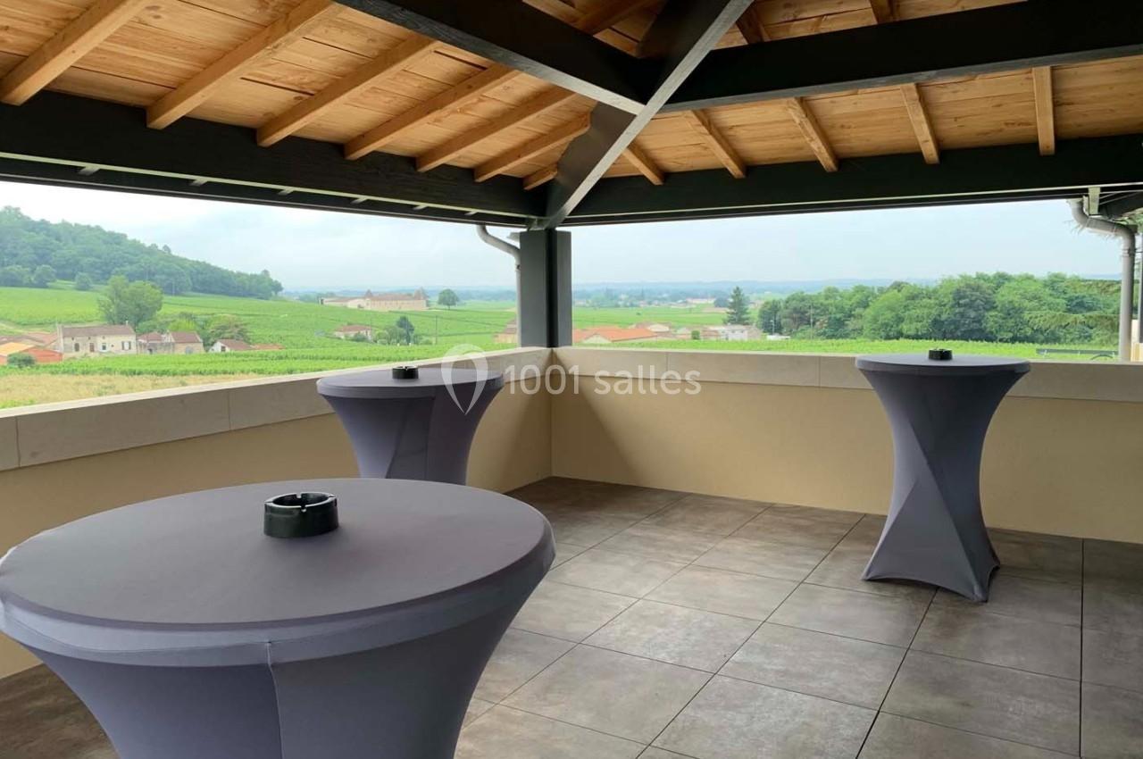 Terrasse couverte avec vue sur des vignobles, équipée de tables hautes drapées de housses grises.
