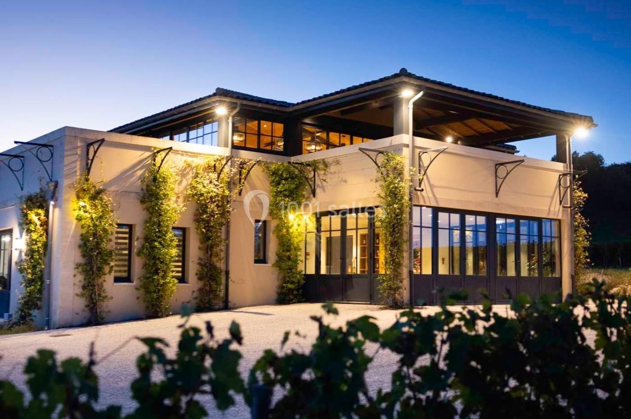 Bâtiment moderne éclairé au crépuscule, entouré de végétation grimpante et d'une cour dégagée.