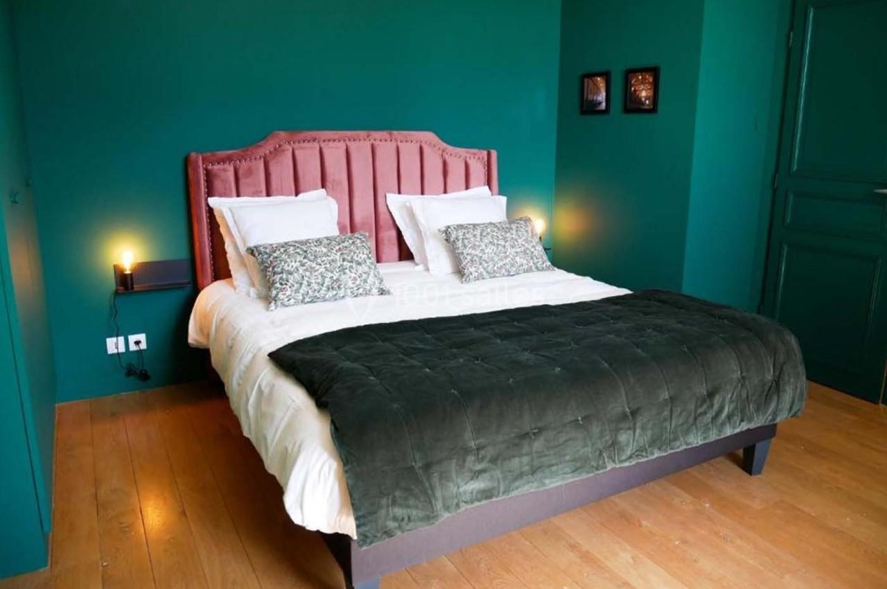 Lit double avec tête de lit rose, draps blancs et couvre-lit vert foncé, dans une chambre aux murs verts.