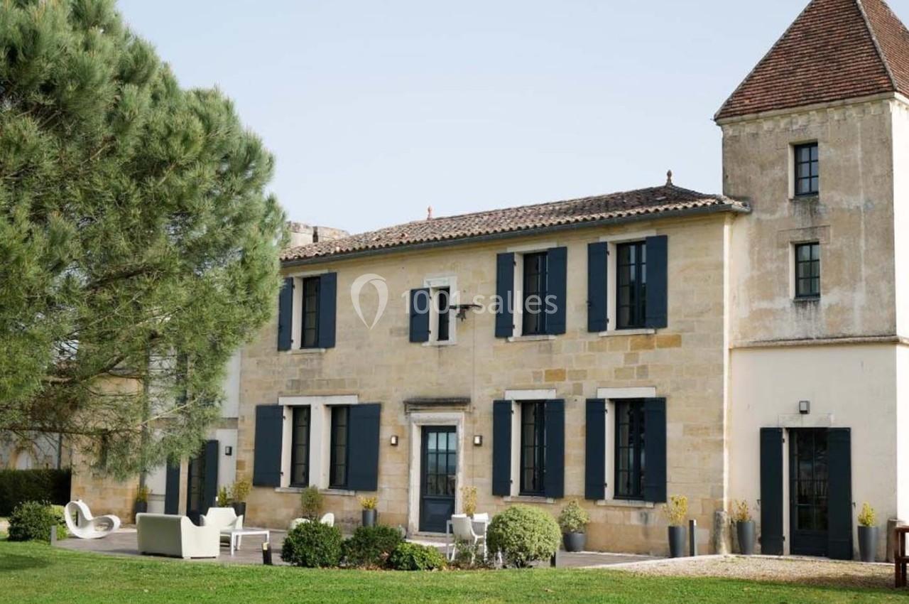 Façade d'une maison en pierre avec volets bleus, une tour attenante et un jardin aménagé au premier plan.