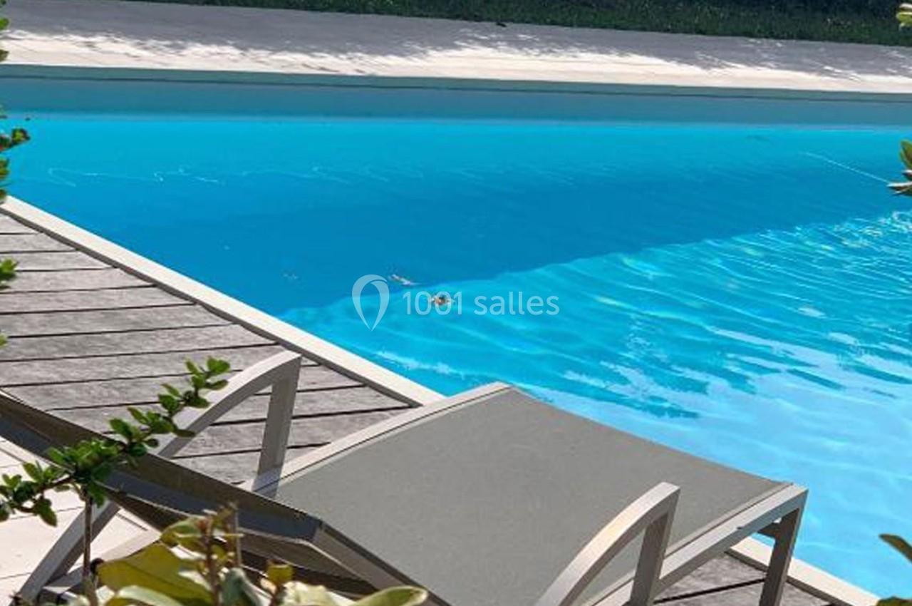 Transat gris clair près d'une piscine extérieure entourée de végétation.