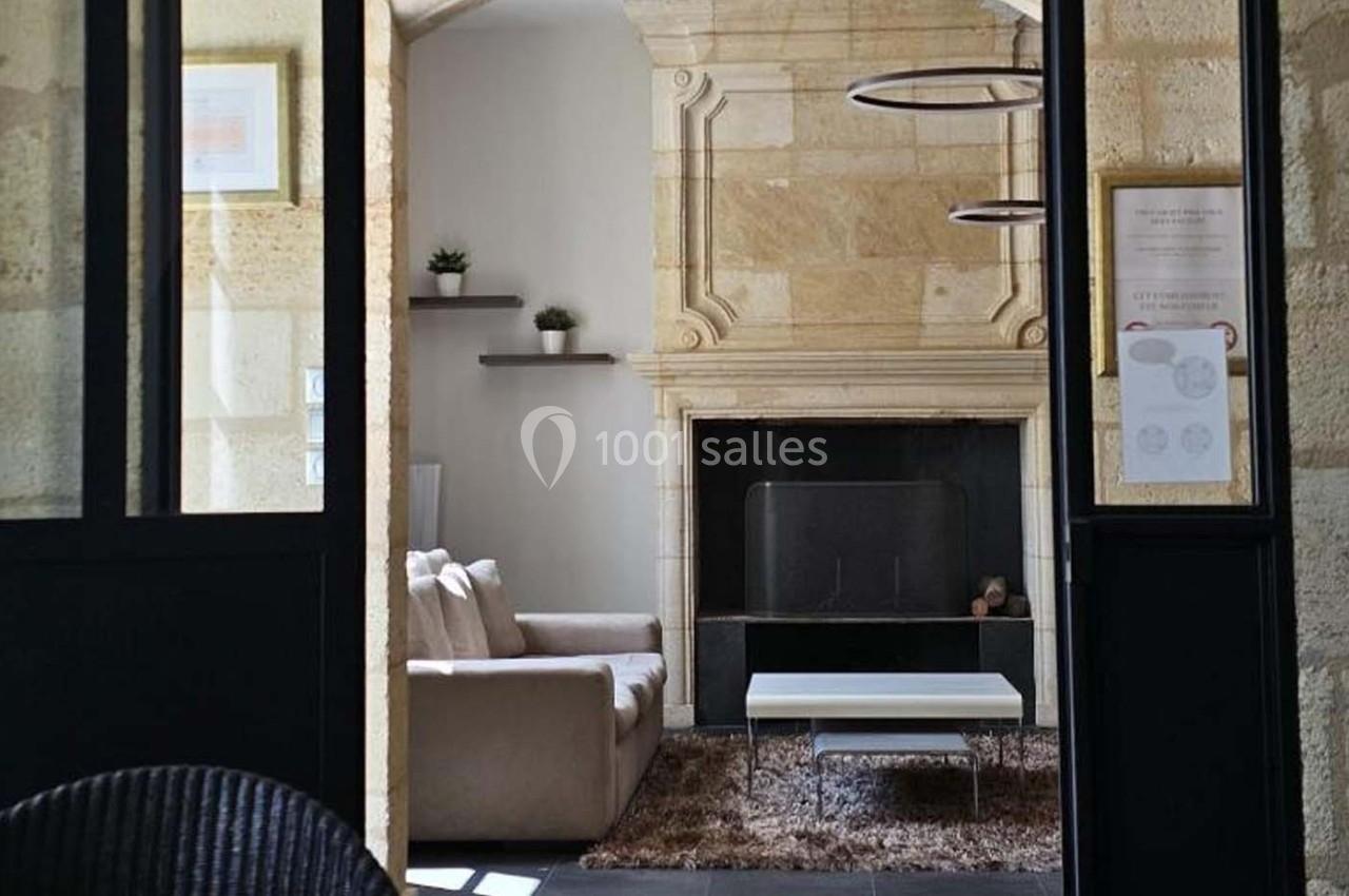 Salon lumineux avec murs en pierre, cheminée, canapé beige, table basse blanche et étagères décorées.